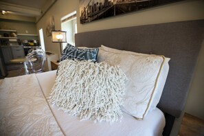 A bed with a textured white throw, a grey upholstered headboard, and a patterned pillow. - Wall Street Suites 3 | Queen Studio near SIU with Kitchen (Carbondale)
