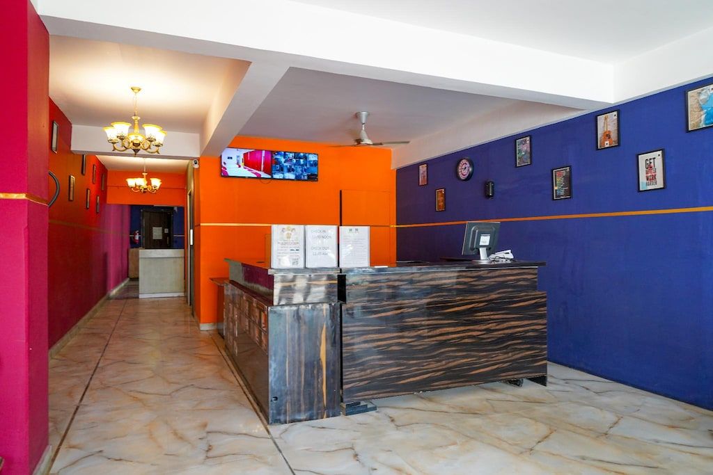 Un vestíbulo de hotel con una recepción, una araña de cristal, un televisor y cuadros en las paredes.