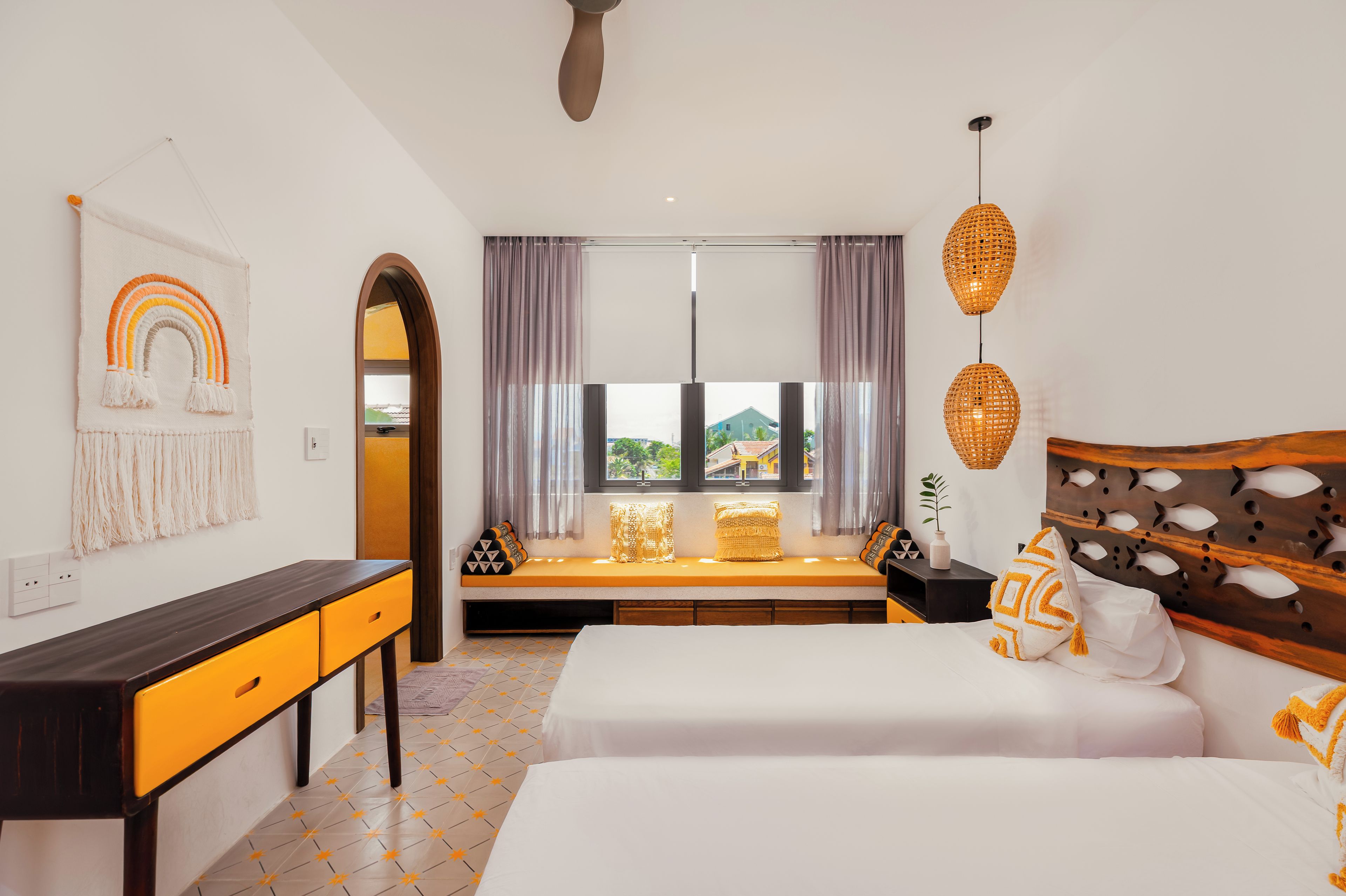 Een hotelkamer met een bed, een bureau, een raam met gordijnen, een muur met decoratie en een plafondventilator.