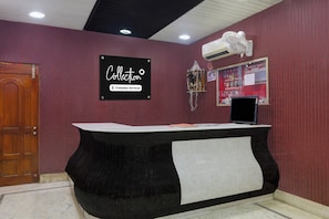 A reception desk with a sign indicating it's company-serviced, a wall-mounted air conditioner, and a bulletin board with various notices.