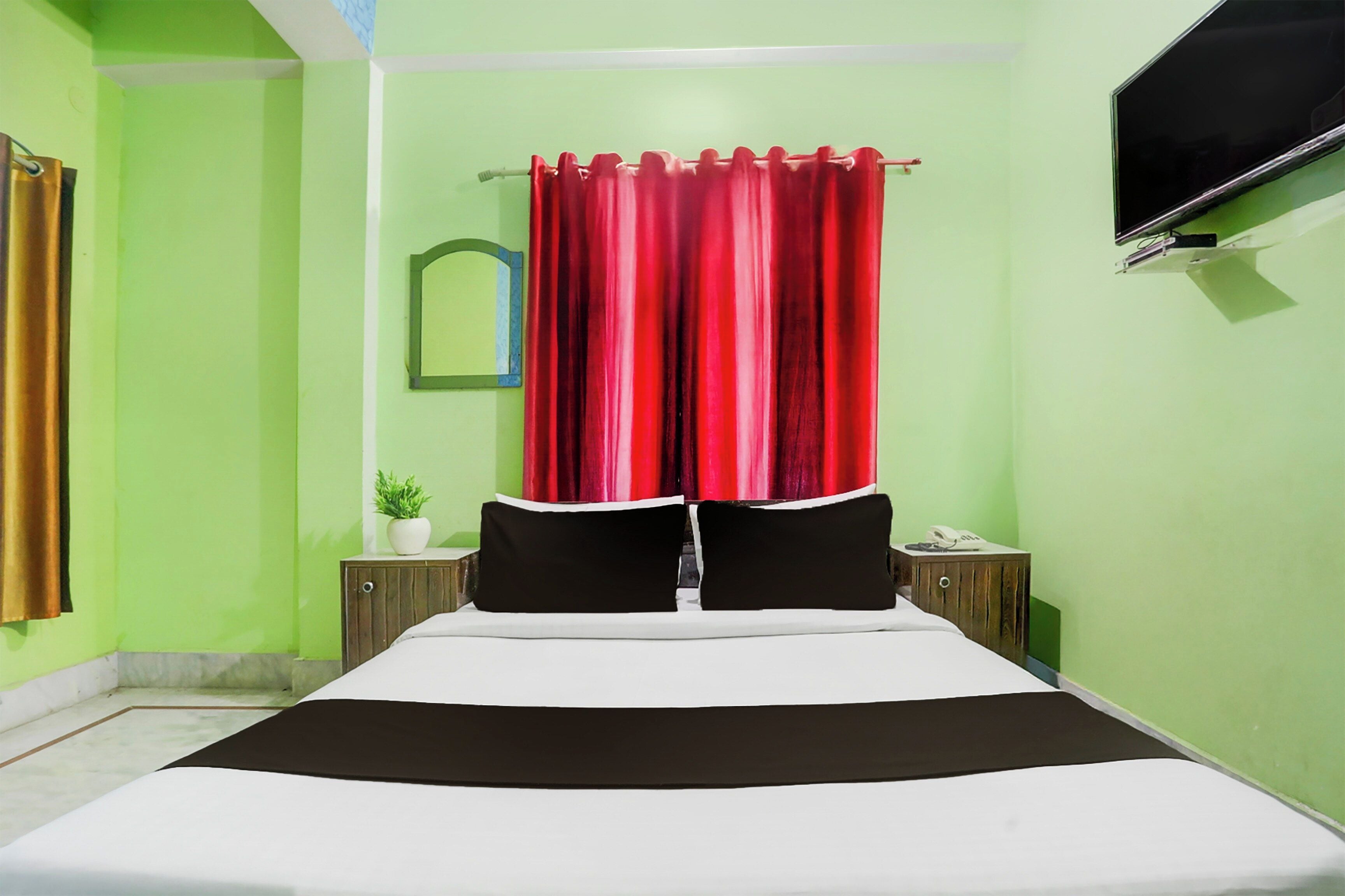A bedroom with a bed, a nightstand, a TV, and a red curtain.