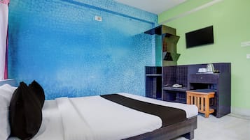 Ett hotellrum med en säng, en liten träpall, en tv som är monterad på väggen och en blå, strukturerad vägg.