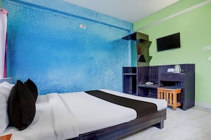 A hotel room with a bed, a small wooden stool, a TV mounted on the wall, and a blue textured wall.