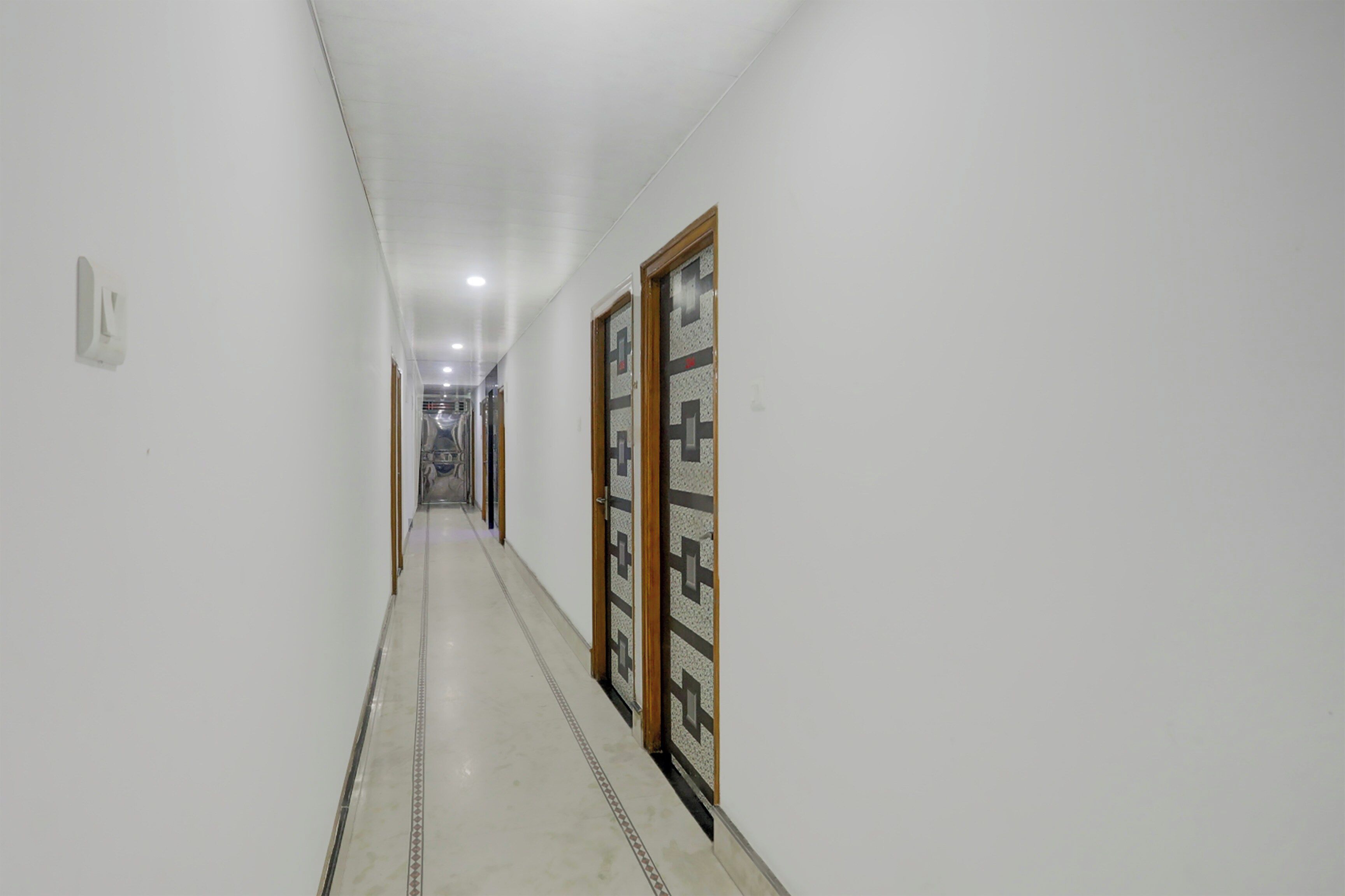 Un pasillo con suelo de baldosas, paredes blancas y una puerta con diseño geométrico.