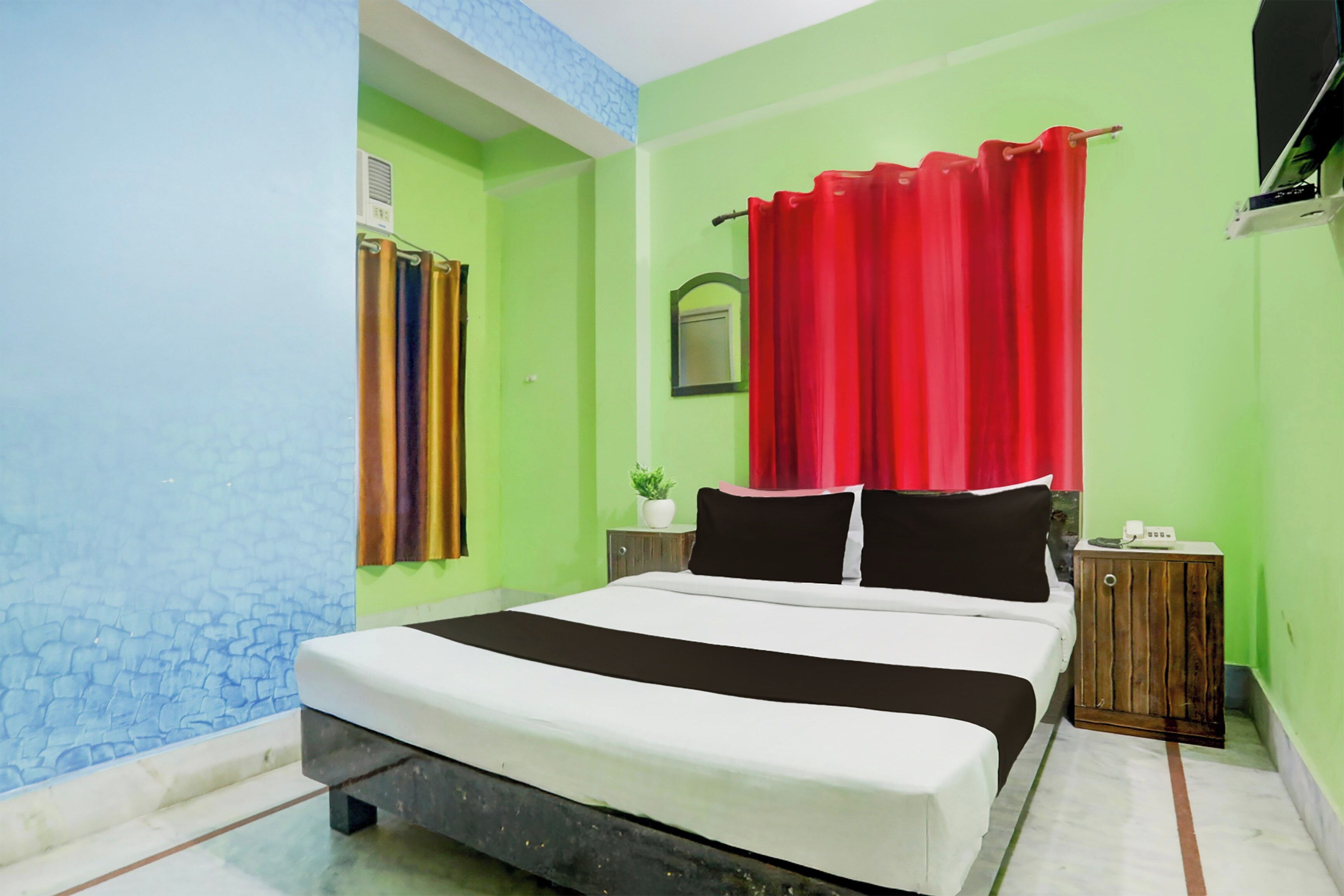 A bedroom with a bed, a nightstand, a potted plant, and a window with curtains.