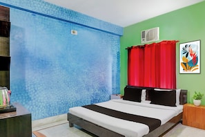 A bedroom with a bed, a nightstand, a wall-mounted air conditioner, and a colorful abstract painting.