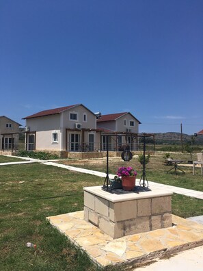 A residential area with houses, a paved walkway, and a stone planter with flowers. - Daphne's Apartment (Kefalonia)