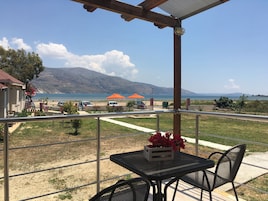 Un balcón con mesa y sillas, con vista a una playa con sombrillas y una montaña al fondo.