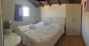 A bedroom with two beds, a wardrobe, a small table with a plant, and a window with curtains. - Daphne's Apartment (Kefalonia)