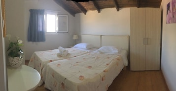 Un dormitorio con dos camas, un armario, una mesita con una planta y una ventana con cortinas.