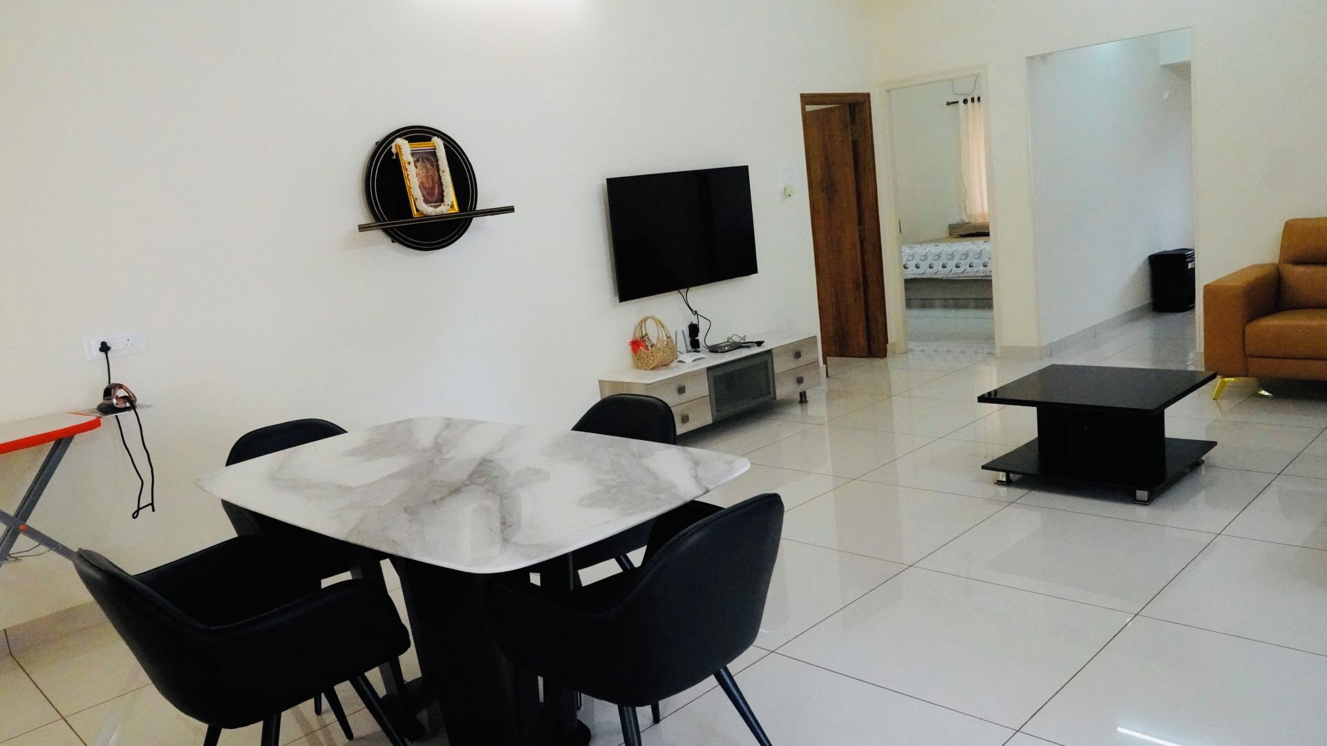 A modern living room with a dining area, a flat-screen TV mounted on the wall, and a sofa.