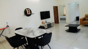 A modern living room with a dining area, a flat-screen TV mounted on the wall, and a sofa.