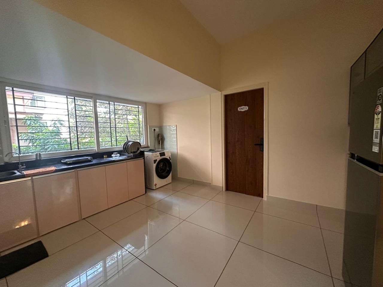 A modern kitchen with a built-in washer and dryer, a large window, and a door labeled 'UNIT 1'.