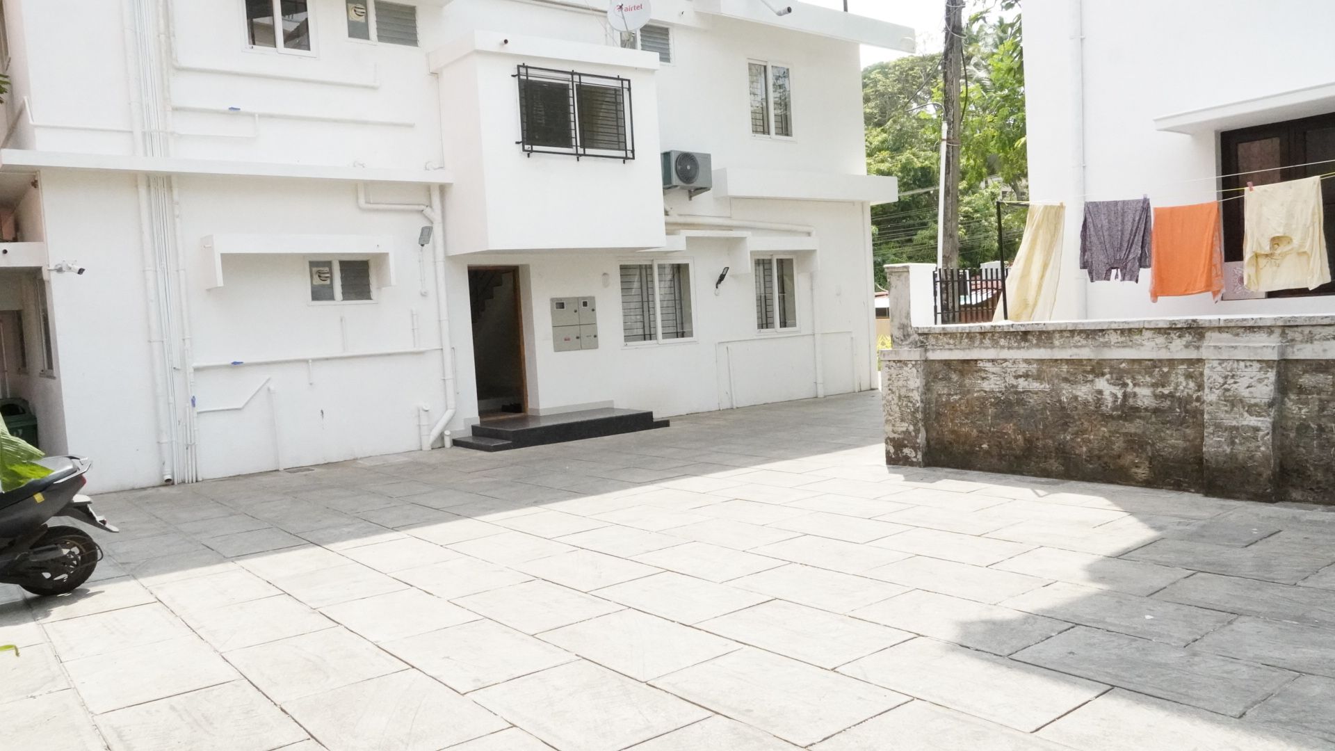 A white building with a tiled courtyard, a motorcycle parked on the left, and clothes hanging on a line to the right.