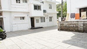 A white building with a tiled courtyard, a motorcycle parked on the left, and clothes hanging on a line to the right.