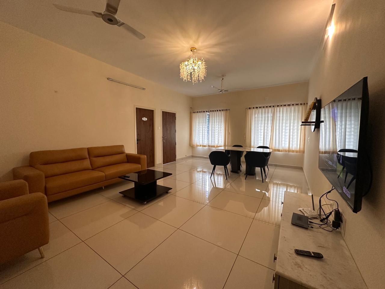 A spacious living room with a sofa, a coffee table, a TV mounted on the wall, and a chandelier.