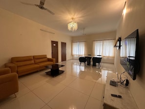 A spacious living room with a sofa, a coffee table, a TV mounted on the wall, and a chandelier.