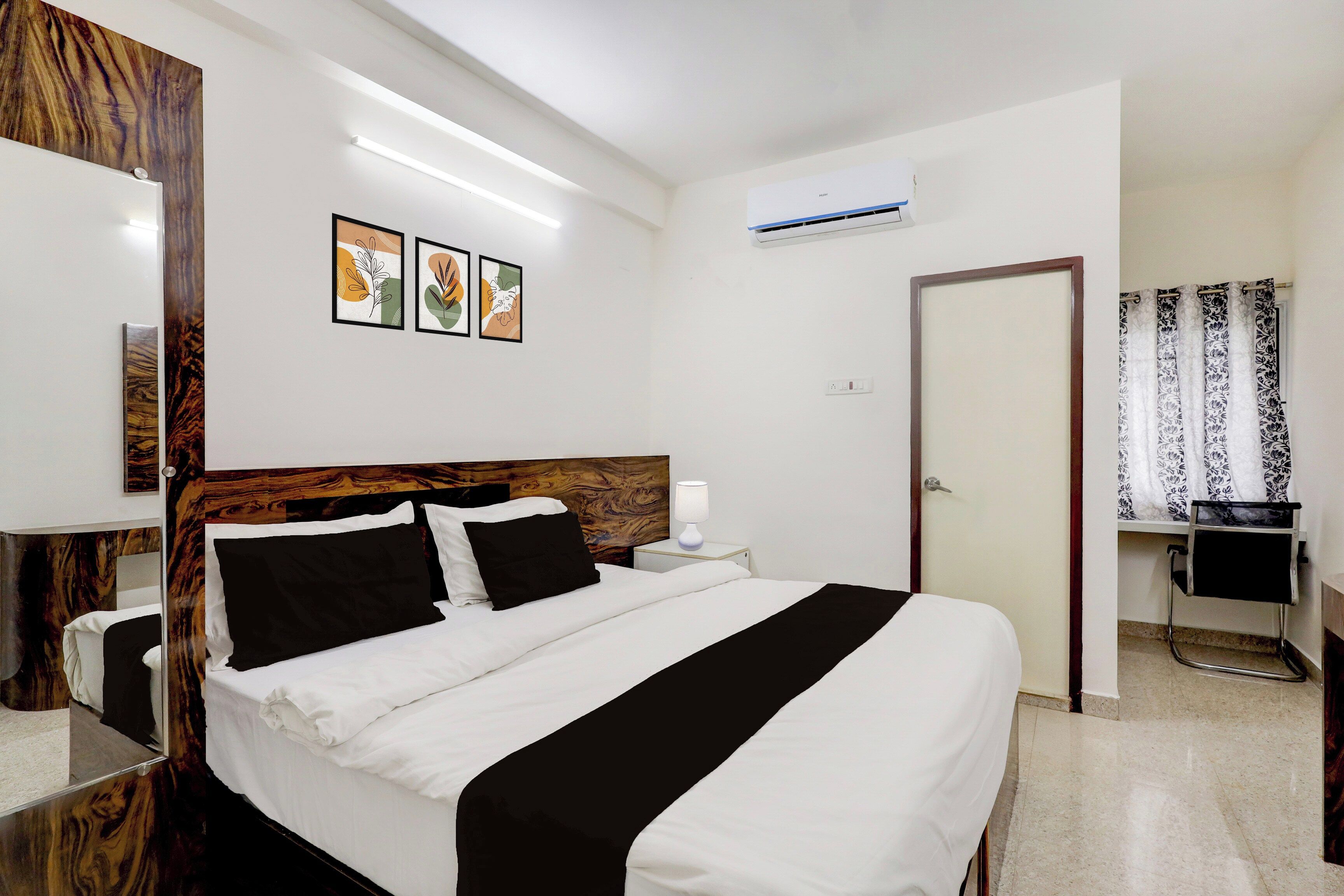 A hotel room with a bed, bedside table, lamp, air conditioning unit, and a door.
