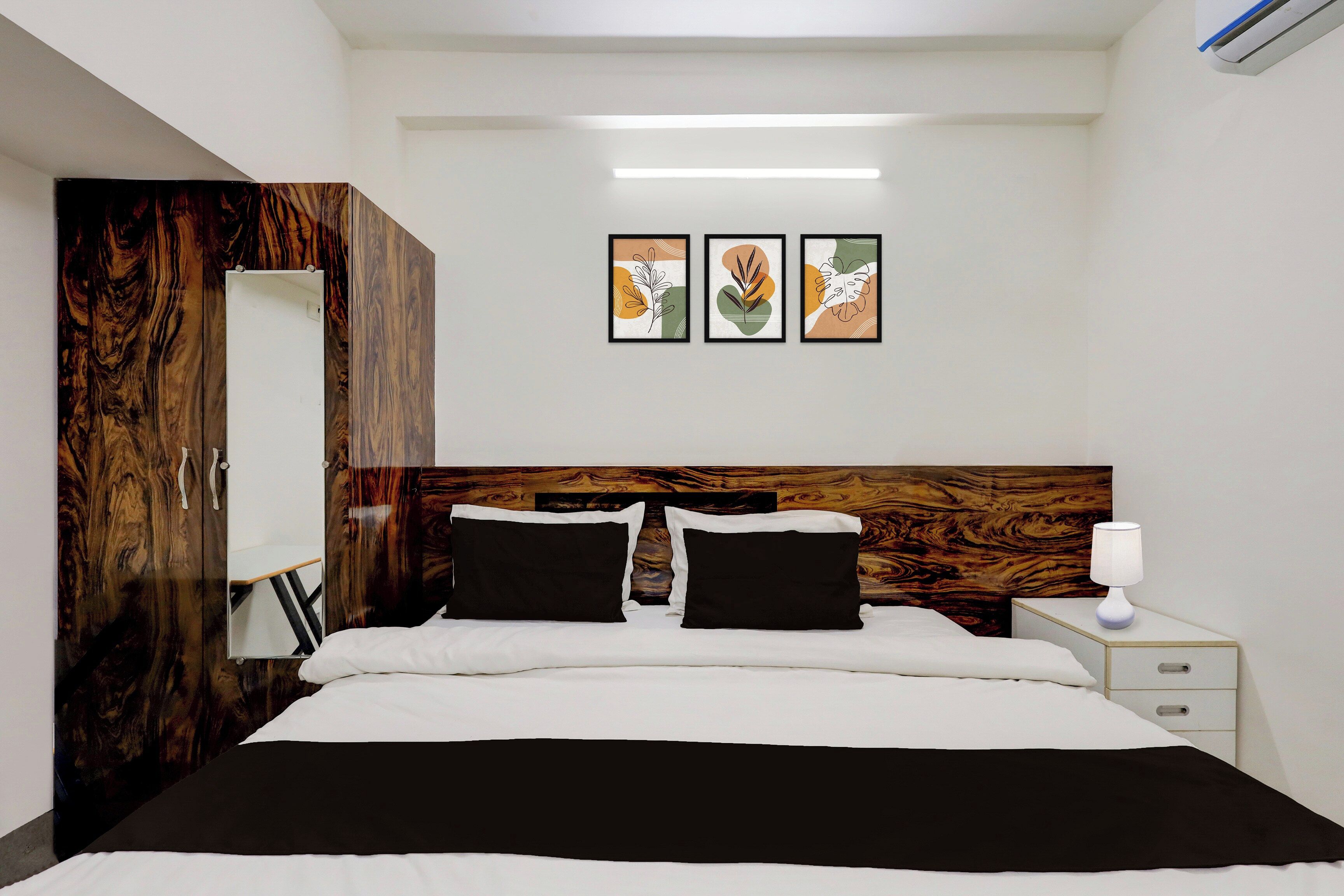 Une chambre d’hôtel avec un grand lit, une tête de lit en bois, une table de chevet avec une lampe et trois œuvres d’art encadrées accrochées au mur.