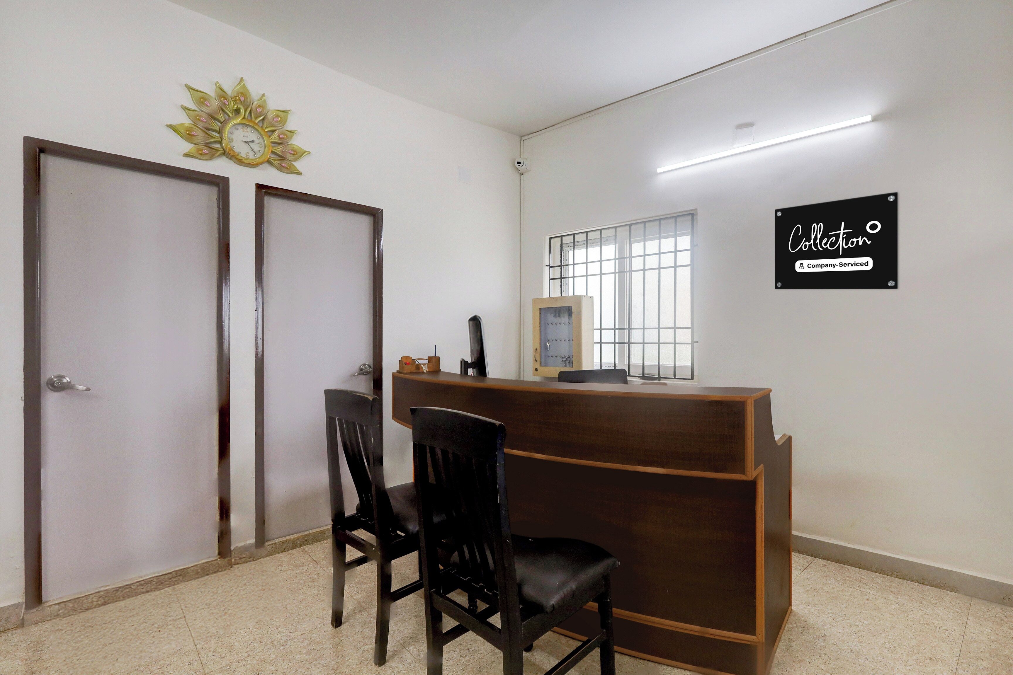 Un'area reception con una scrivania, due sedie, un orologio a muro, una telecamera di sicurezza e un cartello che indica che l'area è gestita dall'azienda.