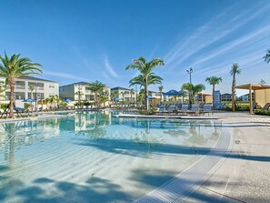 A clear swimming pool with lounge chairs and palm trees, surrounded by multi-story buildings. - Golf Themed 4BR · Private Pool · ChampionsGate (Davenport)