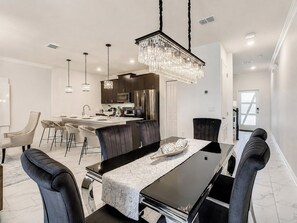 A modern dining area with a black table, white chairs, and a chandelier. - Golf Themed 4BR · Private Pool · ChampionsGate (Davenport)