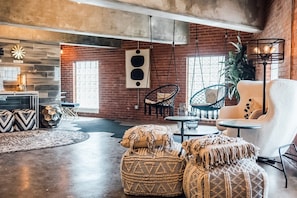 A spacious living area with a brick wall, hanging chairs, a round table, and a sofa. - Wall Street Suites 1 | King Suite near SIU with Kitchen (Carbondale)