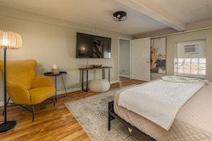 Une chambre à coucher avec un lit, une chaise, une télévision, un tableau et une fenêtre.