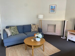 A living room with a blue sofa, a wooden coffee table with a vase of flowers, a standing lamp, and a fireplace. - Frem01 (Fremantle)