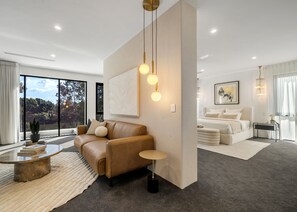 Quarto de hotel moderno com uma janela grande, um sofá, uma mesa de cabeceira e uma cama.