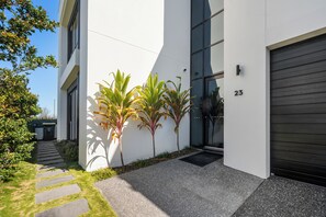 A modern building with a garage door, a number 23 sign, and a small garden with plants. - Riverfront Retreat : Pool, Cinema & Putting Green (Benowa)