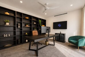 Uma sala de estar moderna com uma estante de madeira escura, uma televisão de tela plana, uma escrivaninha com cadeira e uma poltrona verde.