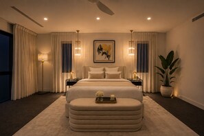 Quarto moderno com cama grande, abajures, luminária de chão, planta em vaso e uma obra de arte emoldurada na parede.
