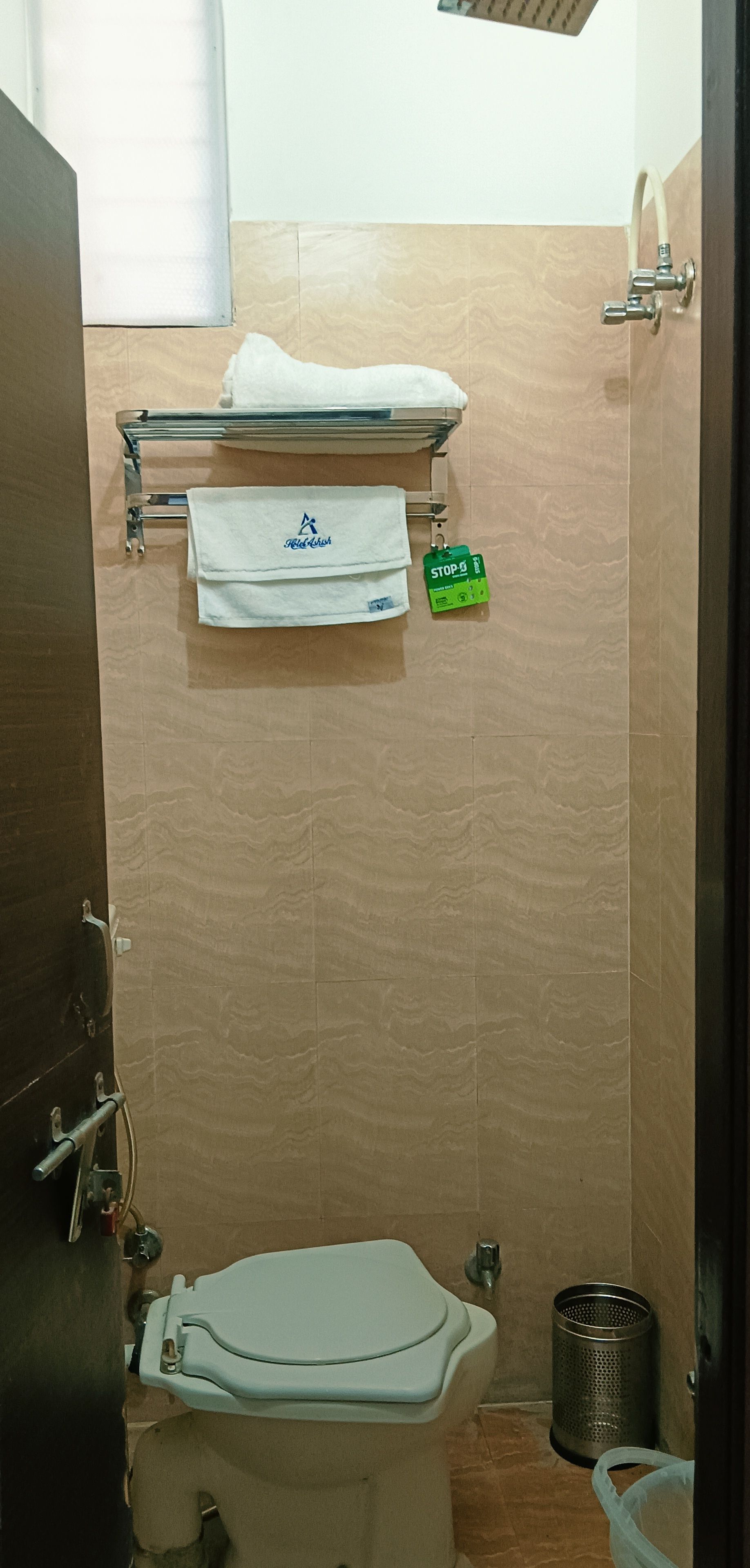 Une salle de bain avec des toilettes, un porte-serviettes sur lequel est pliée une serviette, un bouton d’arrêt vert et une poubelle.