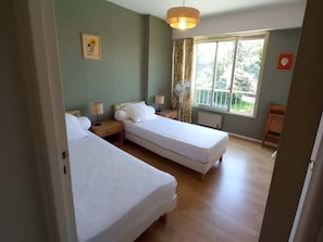 A room with two single beds, a window with curtains, a fan, and a picture on the wall. - Holiday Apartment With 2 Bedrooms (Antibes)