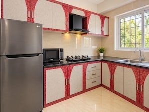 Una cocina con un refrigerador de acero inoxidable, un microondas, una estufa a gas y gabinetes con una combinación de colores rojo y beige.