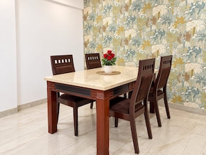 Una mesa de comedor con seis sillas, un jarrón con flores rojas y un papel tapiz floral.