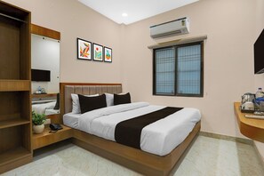 Una habitación de hotel con una cama, una mesita de noche con un teléfono, una planta pequeña, una ventana con persianas y un equipo de aire acondicionado.