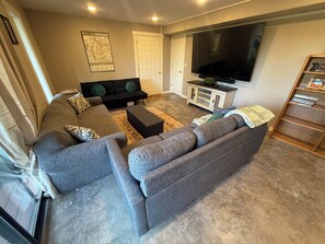 A living room with a grey sectional sofa, a black coffee table, a flat-screen TV, and a wooden bookshelf. - Tranquil 1-bedroom guest suite In Bella Vista Hills (Bella Vista)