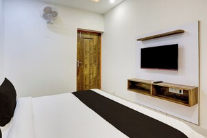 A hotel room with a bed, a wooden door, a mounted TV, and a wall-mounted shelf.