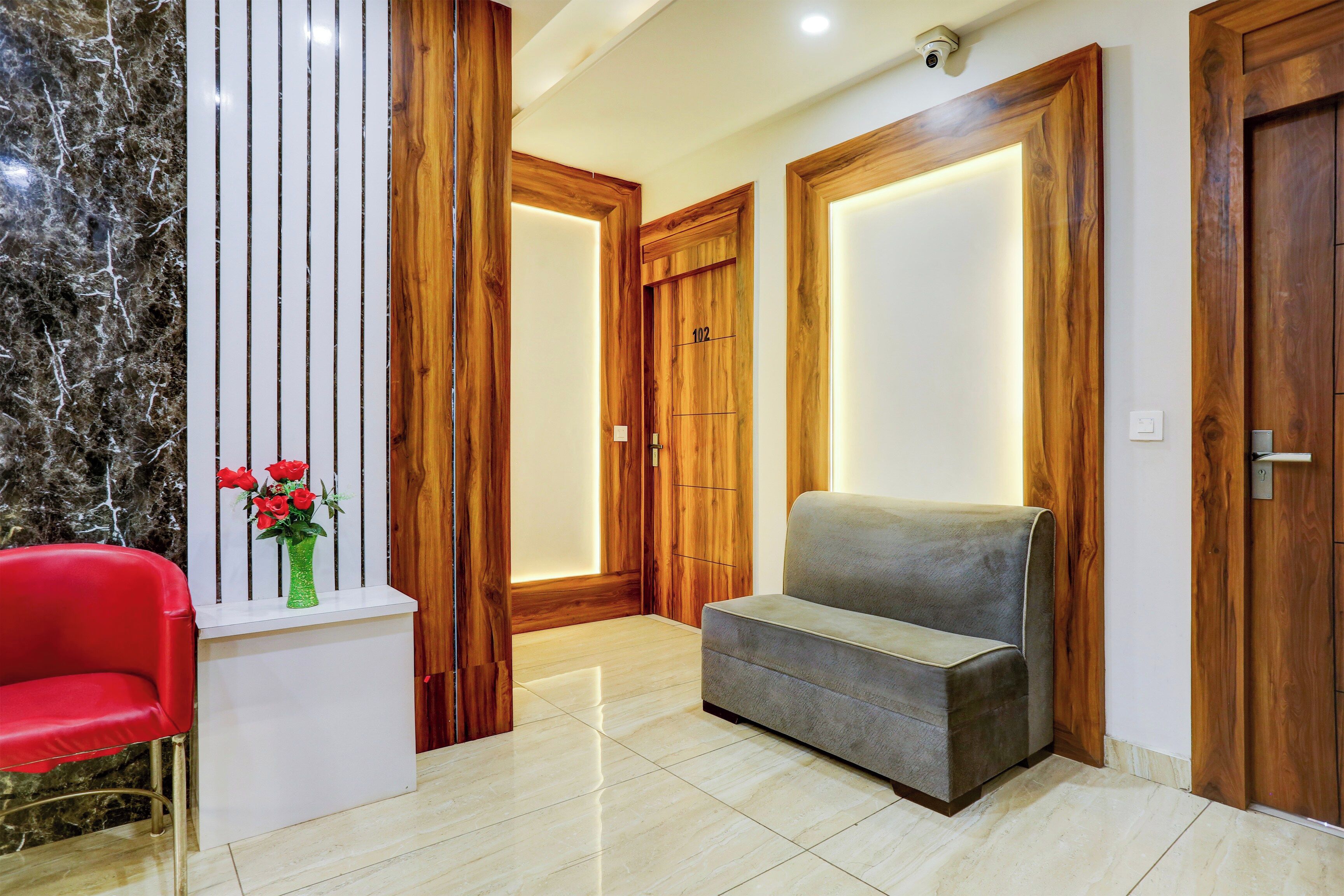 Un interior moderno con una pared de mármol, puertas de madera, una silla roja y un sofá gris.