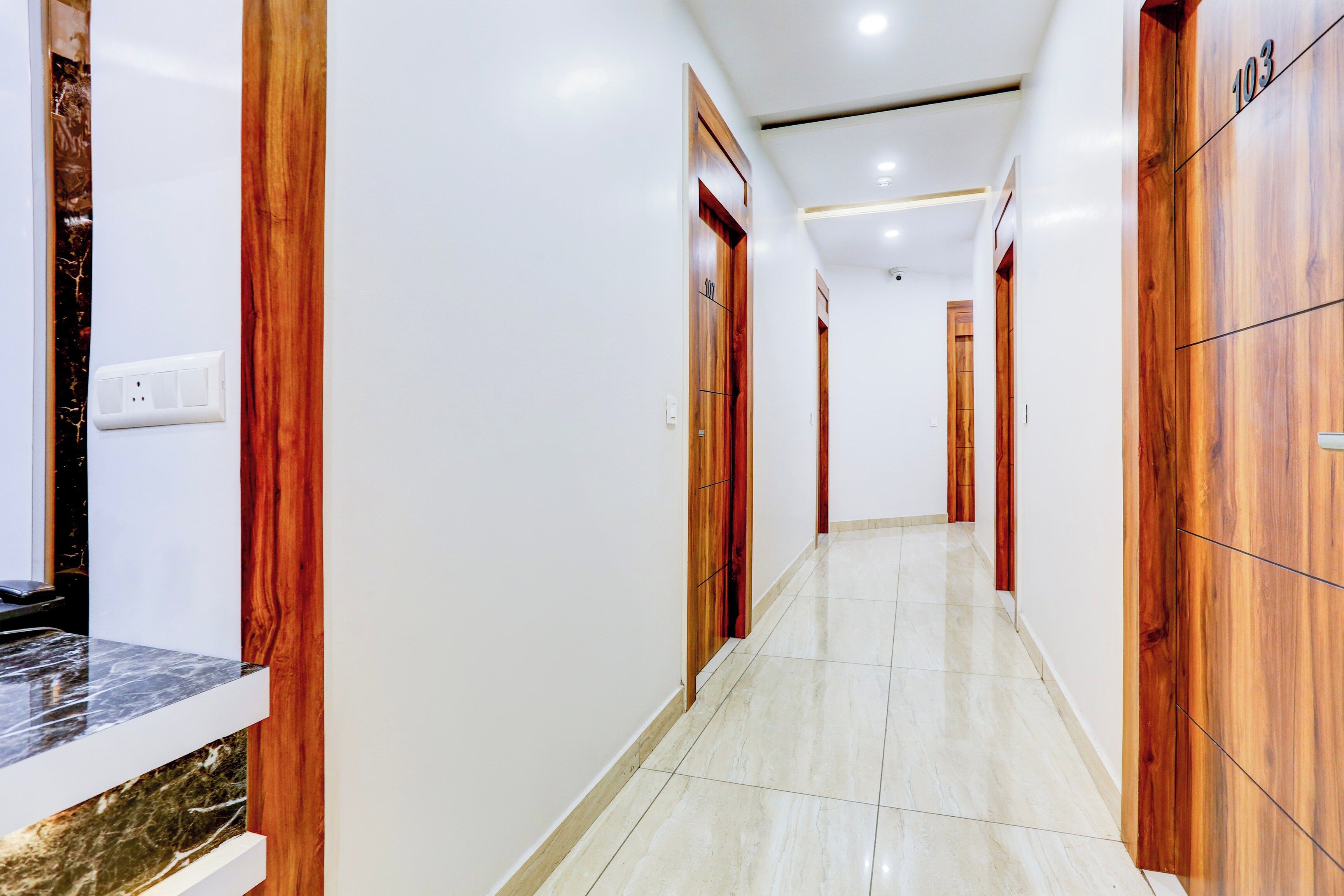 Un pasillo con puertas de madera, piso de mármol y pared blanca.