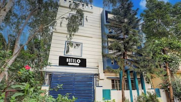 Un hotel con un letrero que indica que ofrece servicios para empresas, una verja azul y varias plantas y árboles alrededor del edificio.