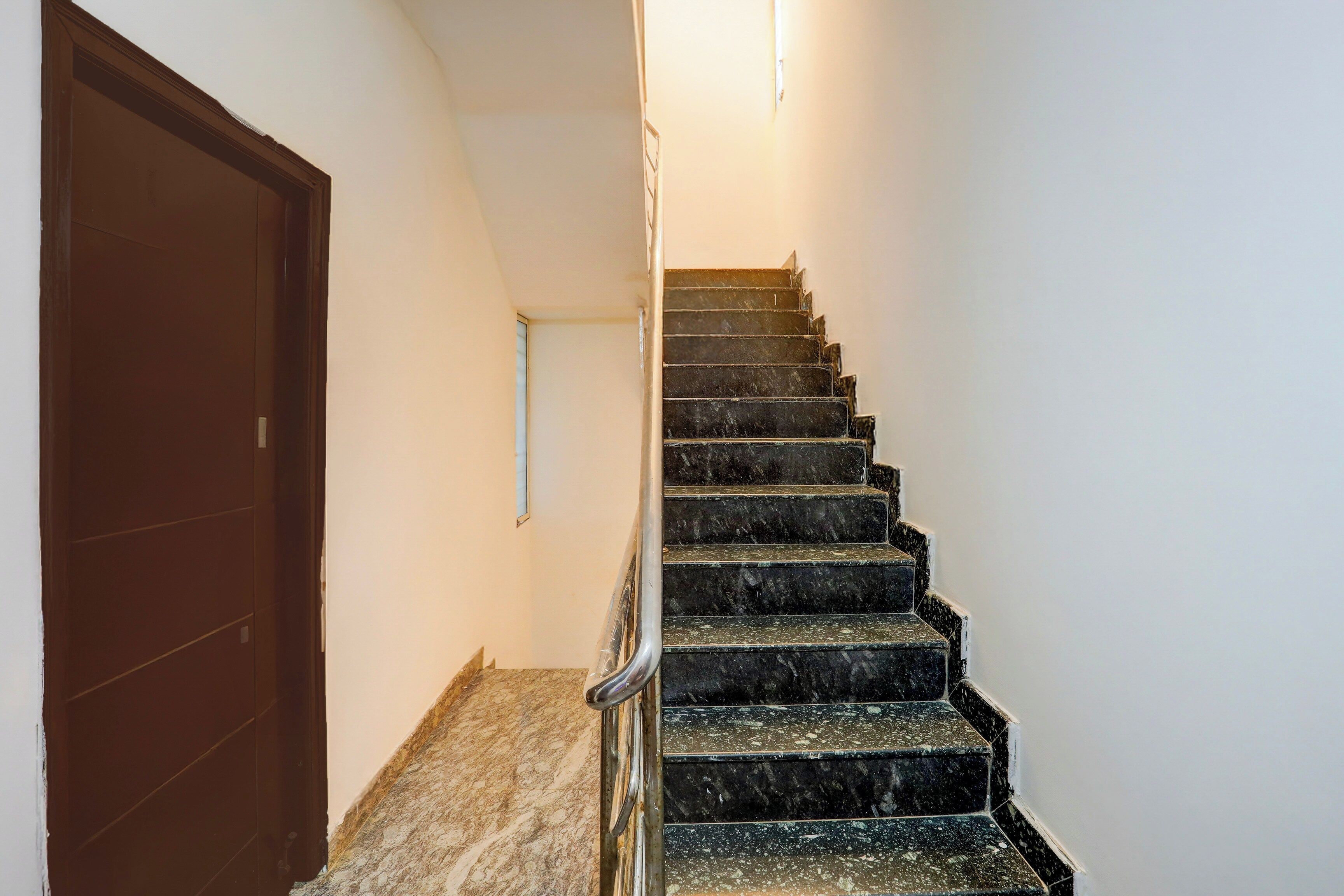 Una escalera con barandilla, una puerta en la parte superior y una lámpara en la pared.