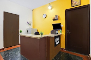 A hotel reception desk with a clock, a small statue, and a sign that reads 'HOTEL & Company Services'. - Hotel O Kogilu Bus Terminal (Bangalore)