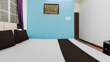 Una habitación de hotel con una cama, una lámpara de pared, un enchufe y una ventana con cortinas.