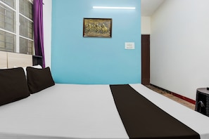 A hotel room with a bed, a wall-mounted light, a power outlet, and a window with curtains. - Hotel O Kogilu Bus Terminal (Bangalore)