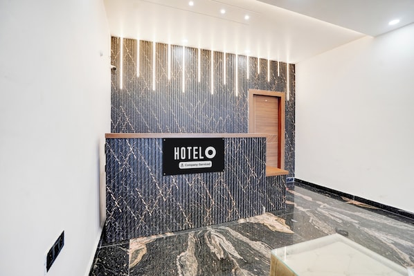 A hotel reception desk with a modern design, a sign indicating it's company-serviced, and a polished marble floor.