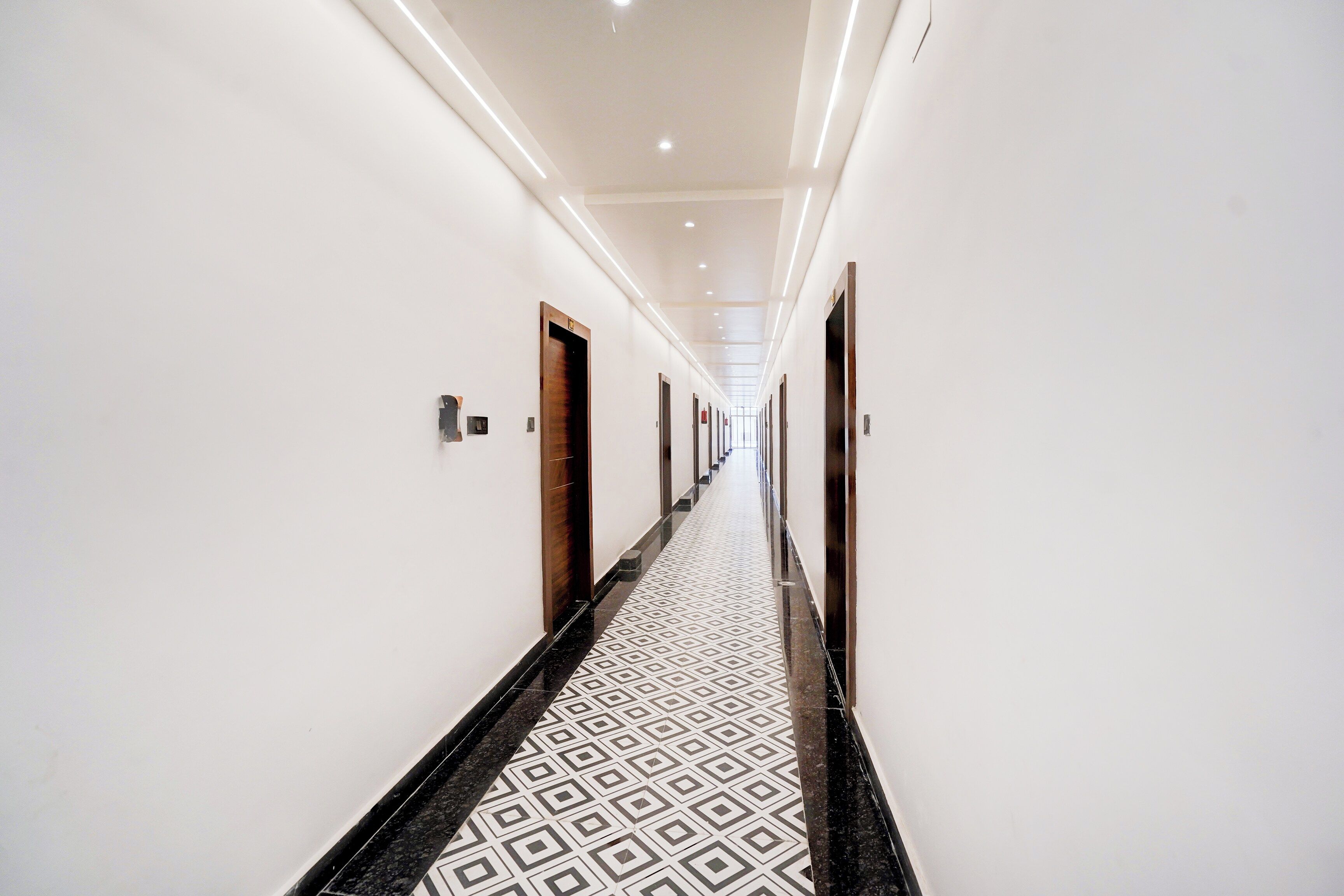 A hotel corridor with a patterned floor, doors, and a ceiling with recessed lighting.