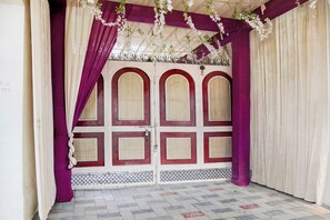 Una habitación con piso de baldosas con diseño, una puerta blanca con detalles rojos y cortinas moradas.